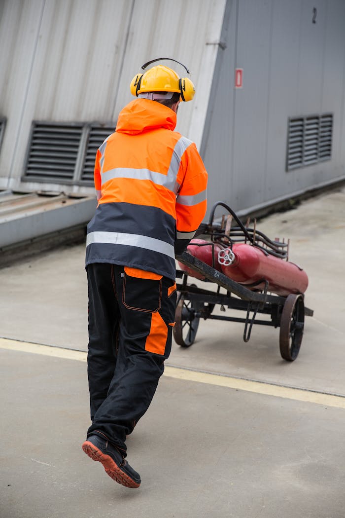 Worker in safety gear transports machinery on industrial site, enhancing workplace safety.
